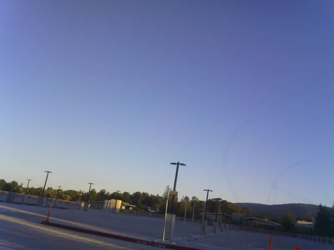 Empty parking lot, mostly sky. Fading golden light of sunset highlights bollards and buildings.