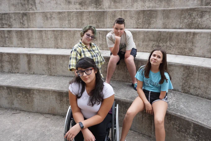 Three people sit on cement steps. One person is sitting in a wheelchair.