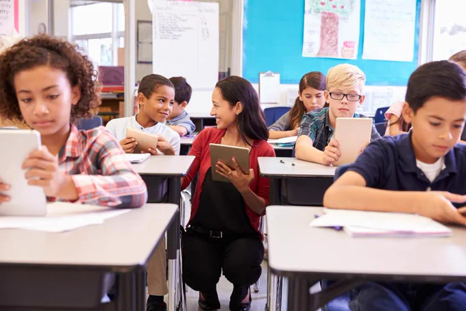 Stock photo. Teacher works with students in a class who are learning on tablets. 