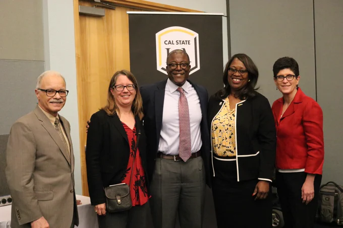 Five individuals standing in front of a Cal State LA banner and posing for the camera. Dr. Sello in the middle.