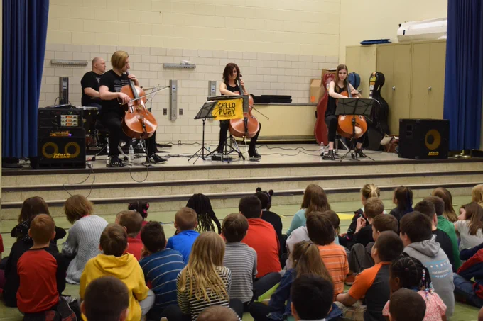 three cellists and drummer on stage with children in audience
