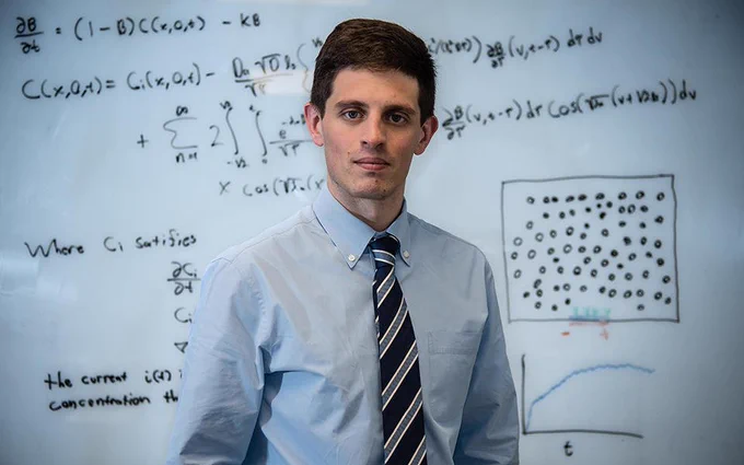 Mathematician Ryan Evans in front of a whiteboard covered in mathematical equations.