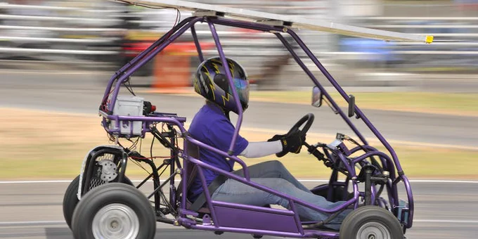 Photo of a person in a purple go-kart whizzing by.