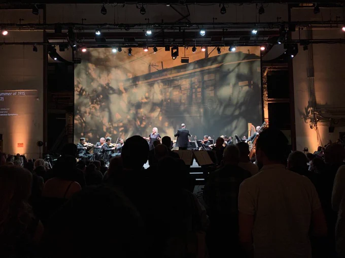Soprano Marnie Breckenridge and members of the SF Symphony perform Knoxville: Summer of 1915, Op. 24, by Samuel Barber, conducted by Christopher Rountree. A streetcar is projected onto the screen behind the orchestra.