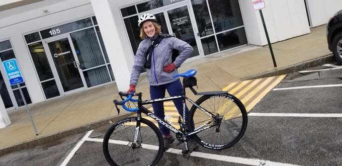Person standing with a bicycle in a parking lot in the rain.