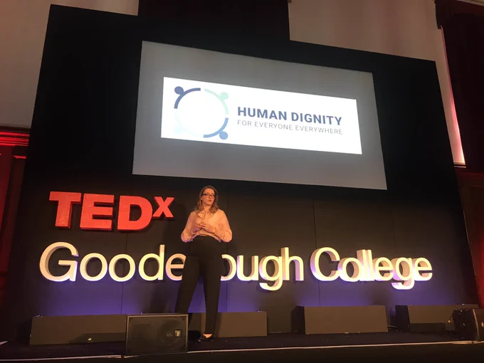 Ewelina on Tedx stage with a slide that says “human dignity for everyone everywhere” at the back