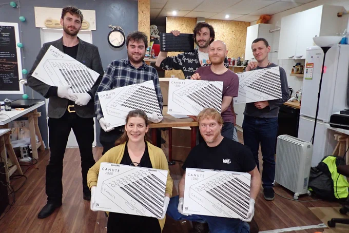 The Bristol Braille Technology team are stood holding Canute 360 boxes in the office. L to R, back to front, Ed, Liam, Jonny, Simon, Zak, Hermione and Russ.
