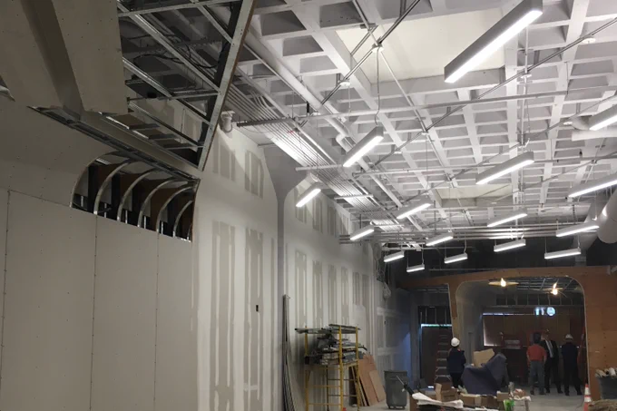 Cafe space under construction with open walls. Linear lights hang from the waffle grid ceiling slab.