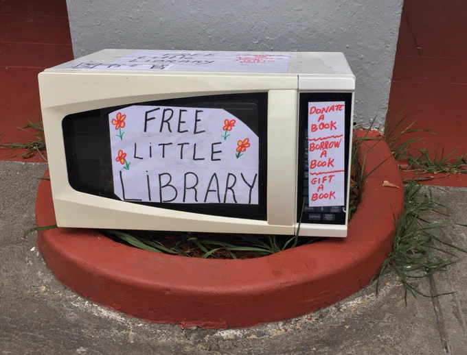 Microwave oven covered in signs that say "free little library" and "donate a book, borrow a book, gift a book"
