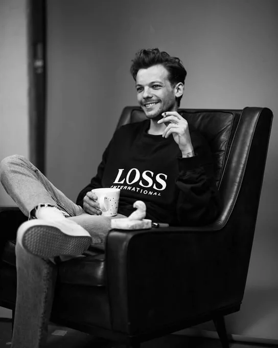 louis sitting on a chair with cigarette on his leaft hand, coffee cup on the right