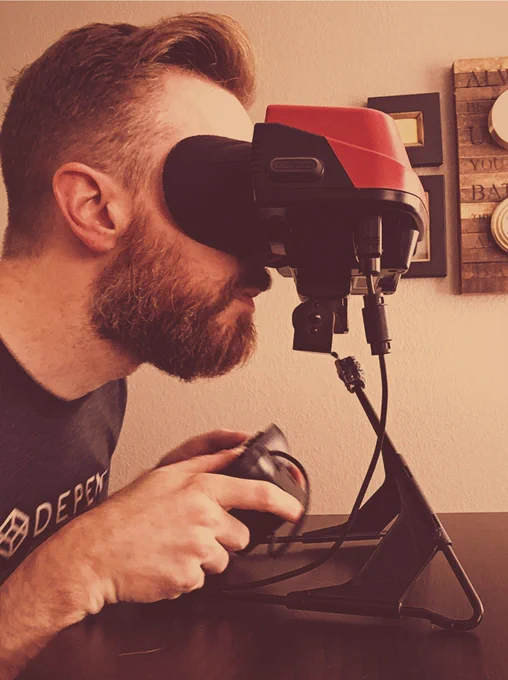 A rugged, handsome bearded man stares into a powered off Nintendo Virtual Boy portable console.