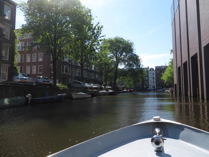 View of canal from boat showing trees  canal houses, boats, cars on shore.