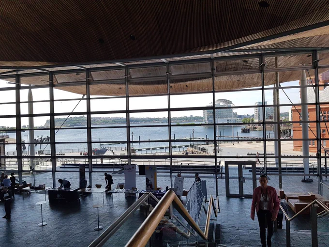 View through a very large window in the front of the Senedd building looking out at Cardiff Bay with red Pierhead building on right hand side