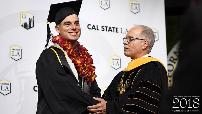 Sean Watkins shakes President Covino’s hand on stage at commencement.