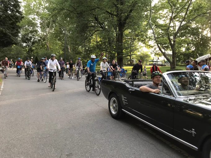 Cyclist ride behind an old mustang car in Central Park on a summery day