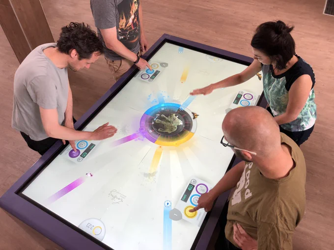 Multi Touch Table, an dem vier Personen spielerisch ein Museumsobjekt vor schädlichen Einflüssen beschützen.