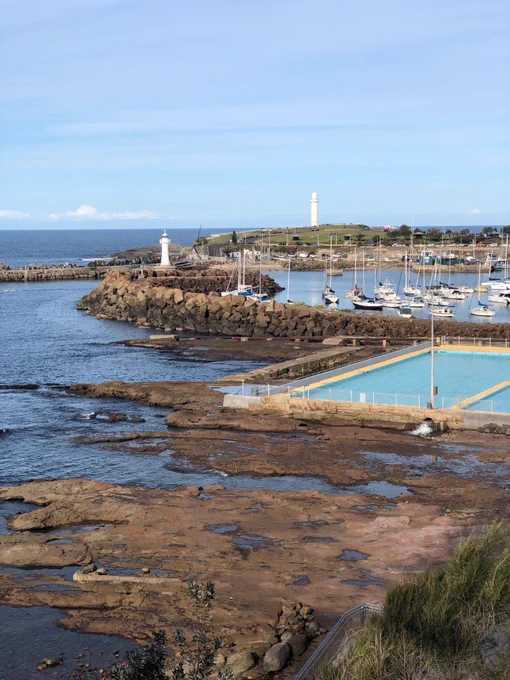 A photo of Wollongong harbour - there are lighthouses in the background, boats and rock pools. It is a clear and sunny day.