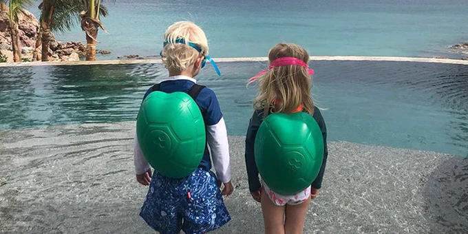 Holly Branson's children stand facing away from the camera modelling the Turtlepack swimming aids stood in front of the pool