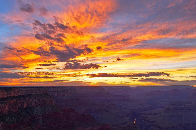 A spectacular sunset over Grand Canyon, with an orange sky filled with clouds over the canyon depths.