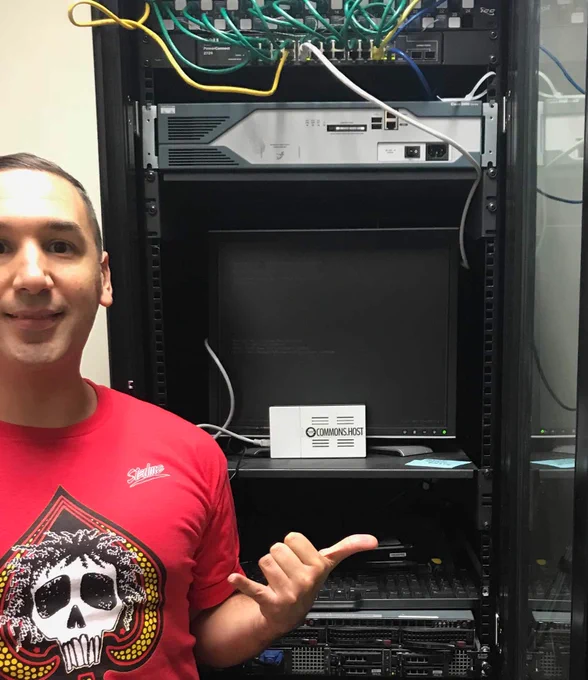 Selfie of Richard Blakely with small Commons Host server in a large server rack.
