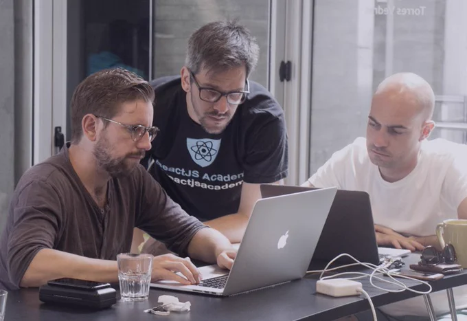 Two men looking a laptops whilst another is behind them inspecting what's on the screen