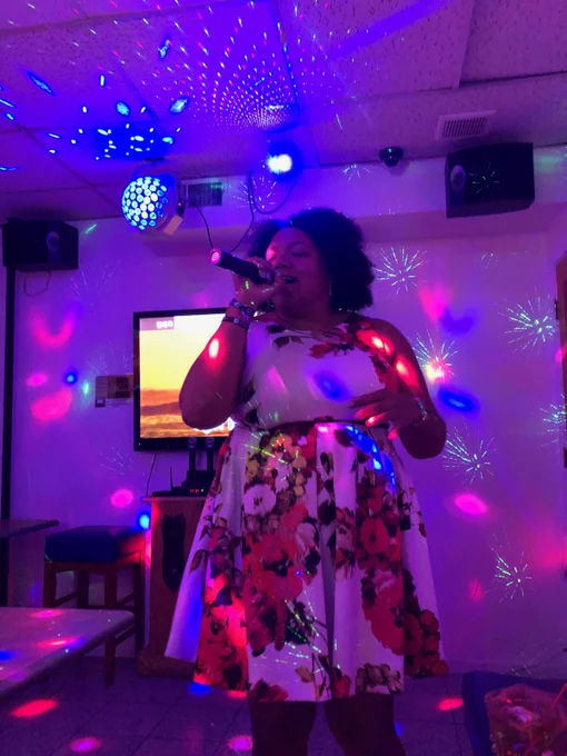 Woman joyfully singing karaoke in a floral dress under multi-colored lights