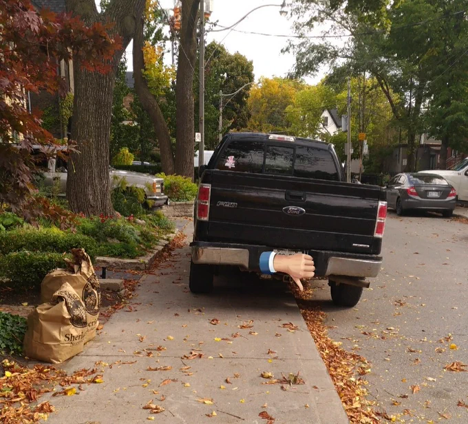 A large pickup truck parked on a residential street with more than half the truck on the sidewalk. In the background, the other cars are parallel parked on the other side of the street, with plenty of room for the truck