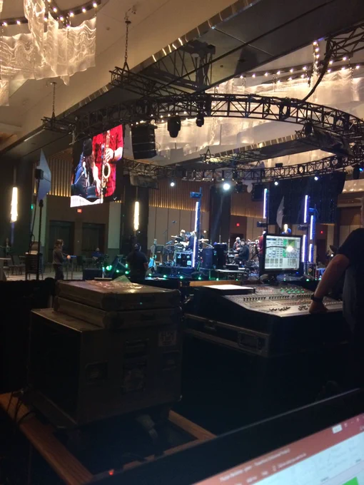Musicians onstage doing a sound check. A computer, soundboard, and other equipment are visible in the foreground