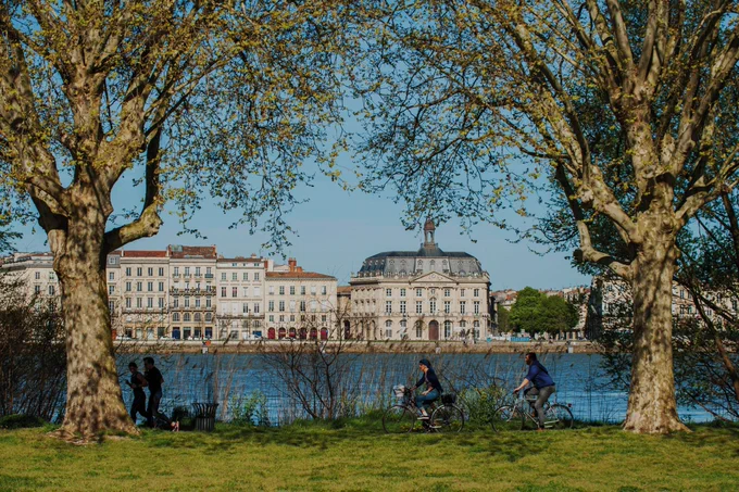 Vue de la place de la Bourse depuis Bordeaux rive droite, des joggers et cyclistes se déplacent sur la piste cyclable, le long de la Garonne.