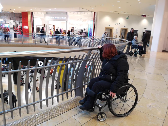 Woman in wheelchair with red hair, overlooking railings at shopping centre