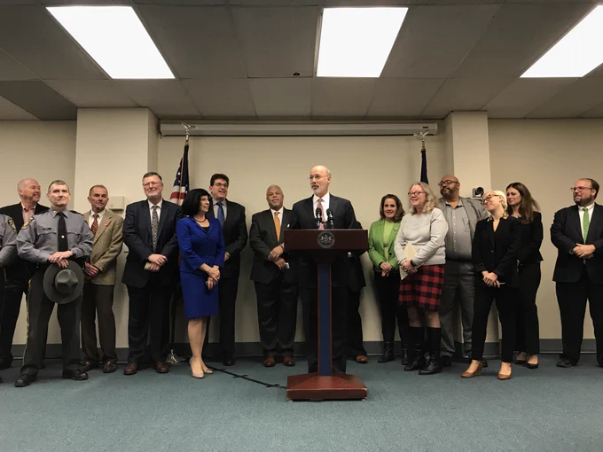 Governor Wolf standing at podium with group of legislators, cabinet members, and law enforcement