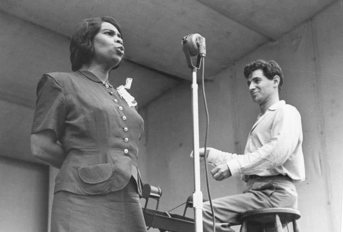 Contralto Marian Anderson stands singing on the Lewisohn Stadium stage as Leonard Bernstein sits on a stool, facing her, conducting. Black and white photo, 1947. 📸 © Ruth Orkin Photo Archive. Used by permission, courtesy of (and thanks to) Mary Engel. All rights reserved.