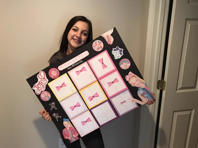 Super cute 9th grader proudly holds poster at an angle.
