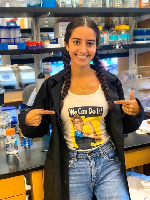 Sara Ricardez Hernandez is standing in a lab, pointing at her shirt that has Rosie the Riveter and the words, "We Can Do It!"