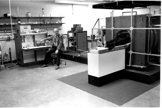Black and white photo of Paul Lauterbur using an original MRI scanner.