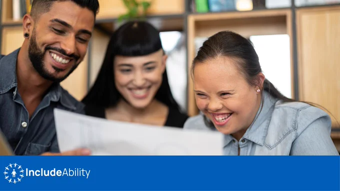 Young woman with Down Syndrome smiling and looking at a document with her male and female colleagues.