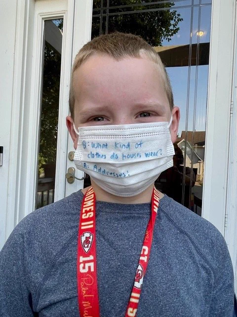 Charlie wearing a mask that has a joke on it. The joke on the mask says, "Q: What kind of clothes do houses wear? A: Addresses."