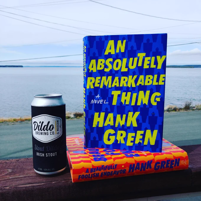 ID: two hard cover books and a can of stout on a railing overlooking the ocean.