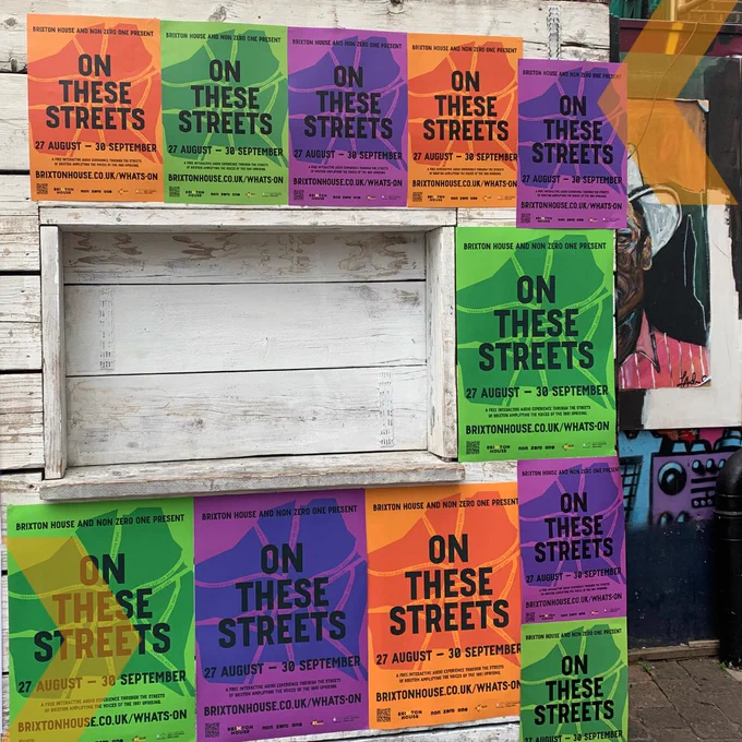 Shed in Brixton Village covered in several posters for ON THESE STREETS. The posters are orange, green and purple and their main feature is a stylised graphic map of the distinctive Brixton triangle alongside the title, dates and website. They are repeated along the shed to create a flyposting effect.