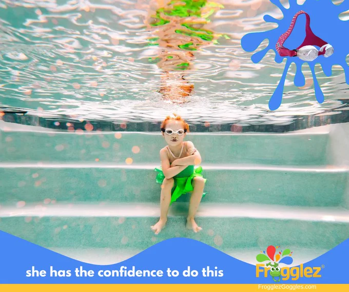 Young girl with red hair sits underwater wearing Frogglez swimming goggles and a bright green Tinkerbell costume with arms crossed. Text reads: she has the confidence to do this