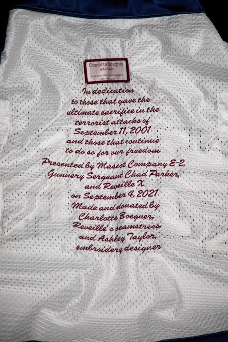 An inscription in the inside of the blanket that reads “in dedication to those that gave the ultimate sacrifice in the terrorist attacks of September 11, 2001, and those that continue to do so for our freedom. Presented by Mascot Company E-2, Gunnery Sergeant Chad Parker, and Reveille X on September 4, 2021. Made and donated by Charlotte Boegner, Reveille’s seamstress and Ashley Taylor, embroidery designer”