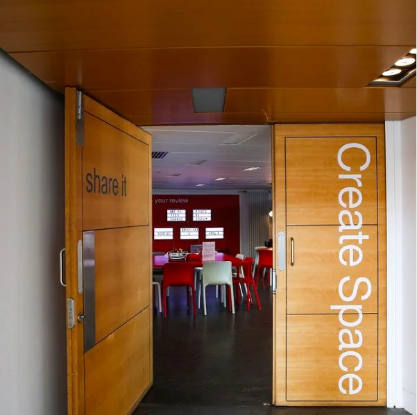 A photograph of a doorway , the left door is open and has the words "share it" written, the right door closed with the words "create space" written.  through the doorway you can see som small plastic chairs , a red table and some art supplies on the table.