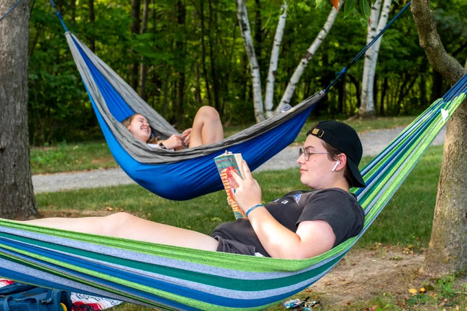Two people hang out in the Arboretum in hammocks slung between trees. 