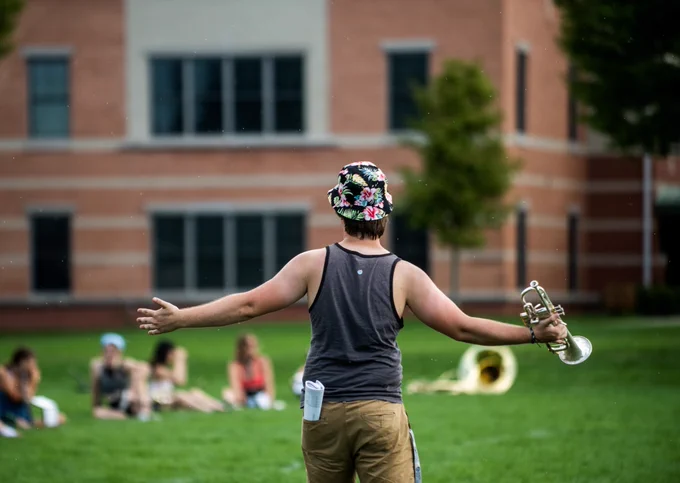A member of the GVSU marching band holds out their arms while holding a trumpet.