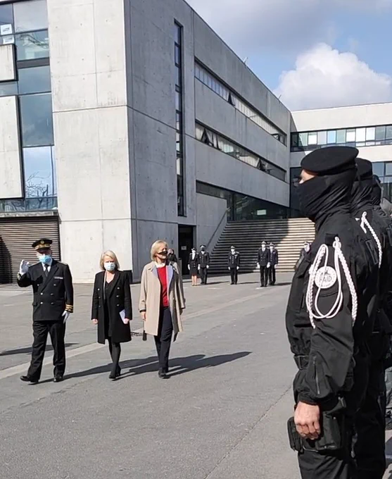 Le préfet et les deux secrétaires d'État à gauche saluent des policiers du RAID à droite. Ils se situent tous en extérieur.