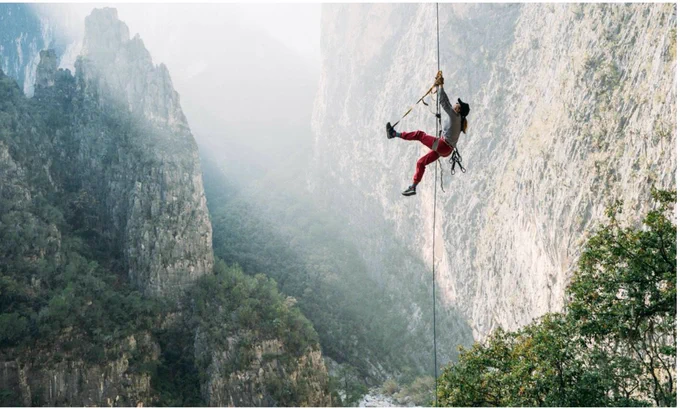 A female rock climber in bright red leggings dangling by cables in a gorge.