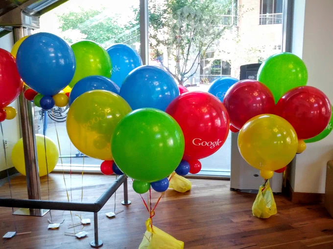 Photo of  three bunches of assorted balloons in red, blue, green, and yellow, with one displaying the word "Google"