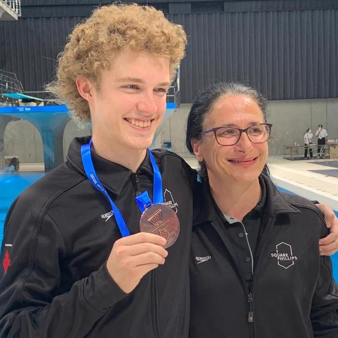 Rylan (left) holds up his bronze medal while doing a side arm hug with his coach for a photo.