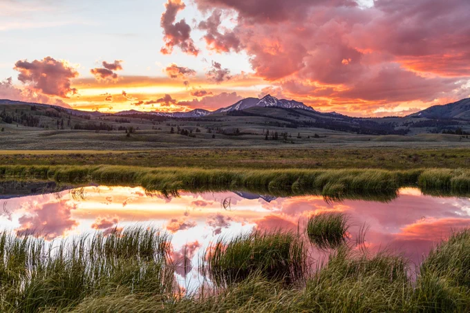 A colorful sunset above a mountain peak reflected in a small pond.