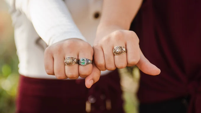 Two people hold their hands out and are wearing class rings. 